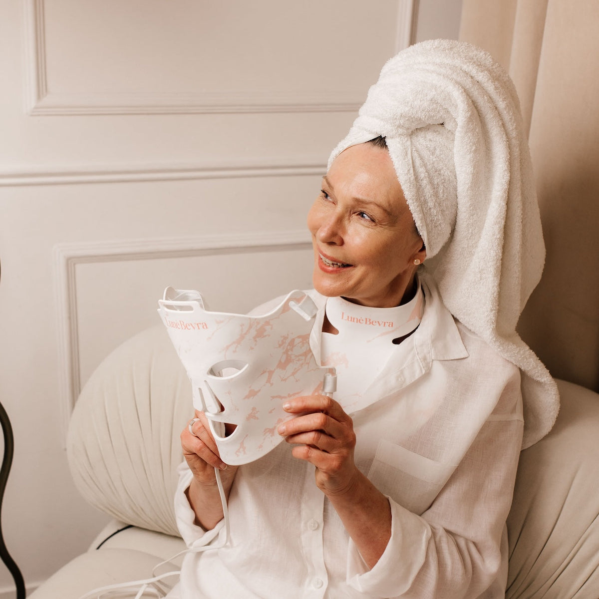 Woman holding the LunèBevra LED face mask with the neck and chest sections in place